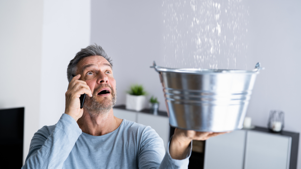 man holding bucket to contain dripping water from ceiling